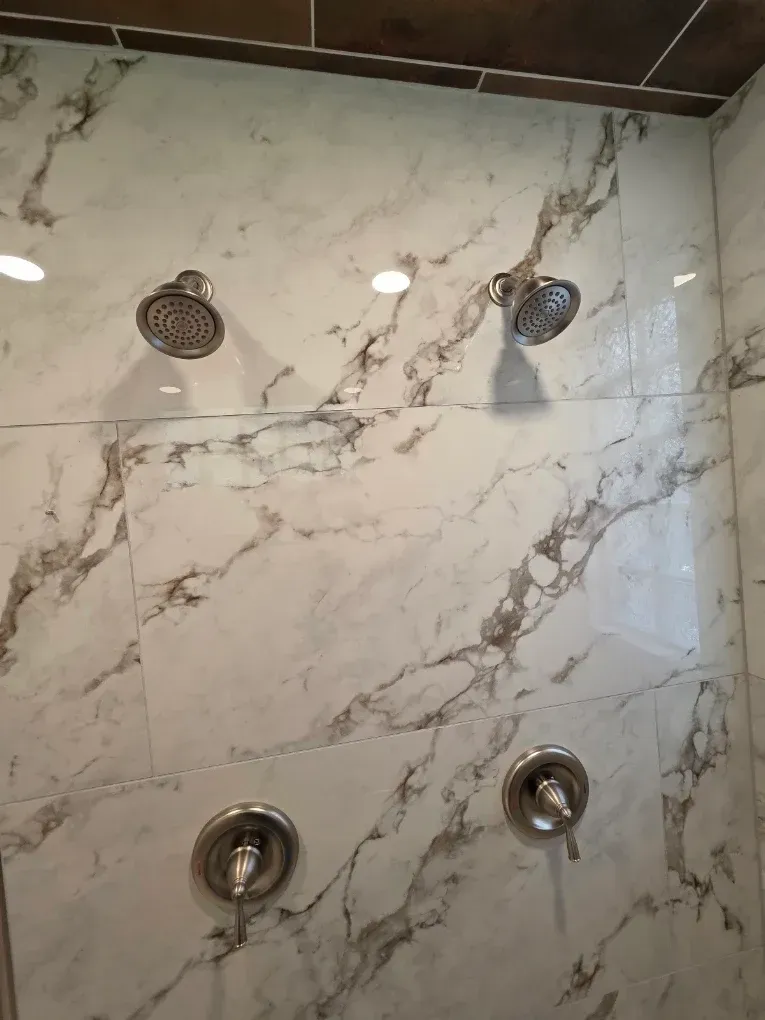 Shower wall with marble-look tiles and four chrome shower fixtures, including two showerheads.
