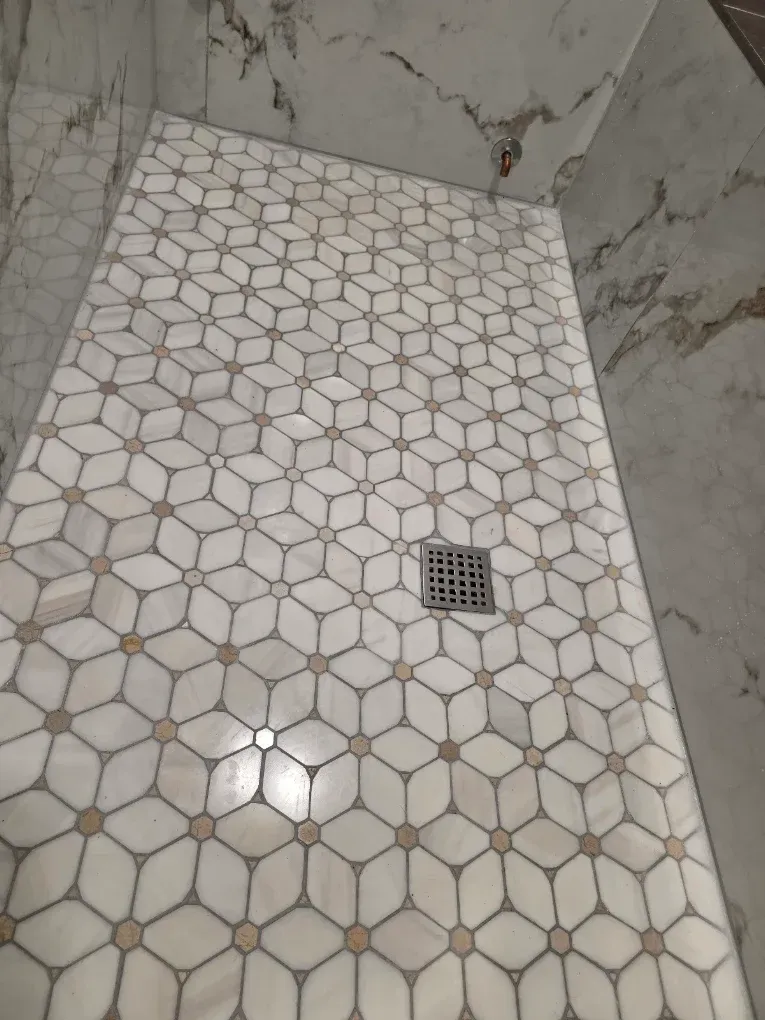 Tiled bathroom shower floor with a drain and light-colored hexagonal tile pattern.